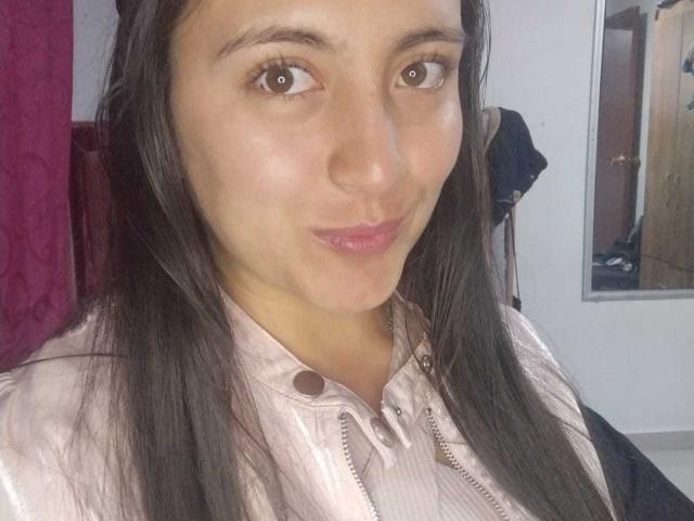 VenusSweetPalmer with long black hair, brown eyes, pink lipstick, and a slight smile, wearing a pink button-up shirt, showing her cute, small, round nose and soft skin.