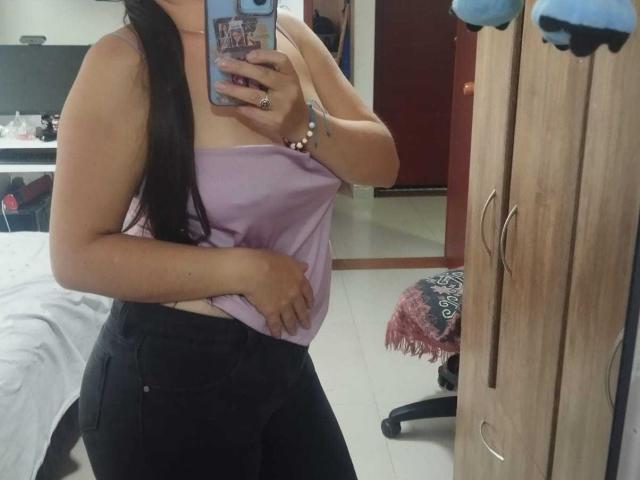 VenusSweetPalmer with long black hair, purple strapless top showing her small tits, black high-waisted pants, holding phone, mirror selfie, wooden wardrobe, bed, and chair in background.