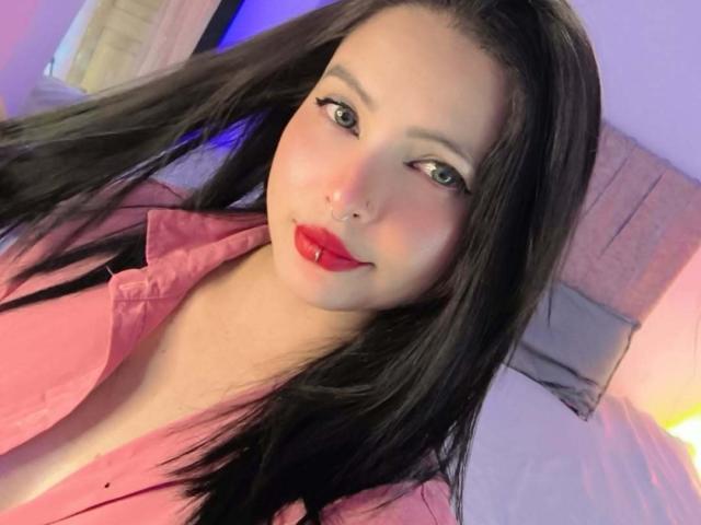 Sofia Leal, met lang zwart haar, rode lippenstift en een neusring, draagt een roze shirt, glimlacht naar de camera, en haar groene ogen kijken rechtstreeks naar de toeschouwer..