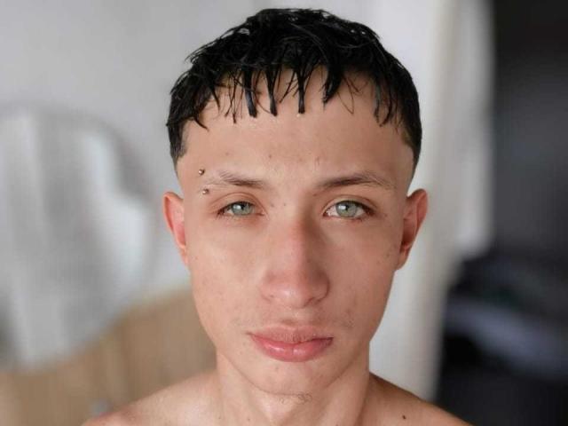 DynamicCouplee has short, wet black hair, pale skin, green eyes, and a small facial piercing on the right side of his nose. He's shirtless with slightly parted pink lips.