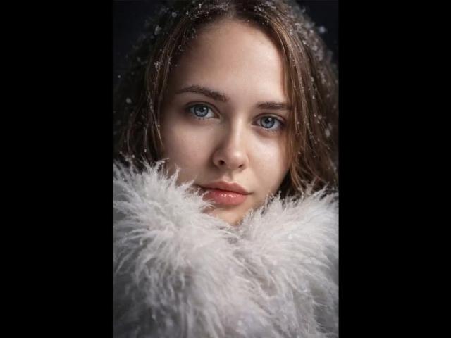 VictoriaAlarie's face with blue eyes, light brown hair, and subtle makeup, partially covered by a fluffy white scarf, showing a serious expression. Snowflakes on her hair.