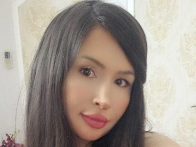 JaneDivine has long black hair, brown eyes, and pink lipstick. Her smooth, tan skin is pretty. She's giving a cute, slightly smirking selfie. Boobs aren't visible.