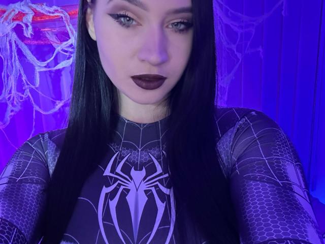 MaryLori with long black hair, wearing a Spider-Man suit, purple blue lighting, dark lipstick, and hexagon patterns, showing off her tits in a tight, black, web-patterned outfit.
