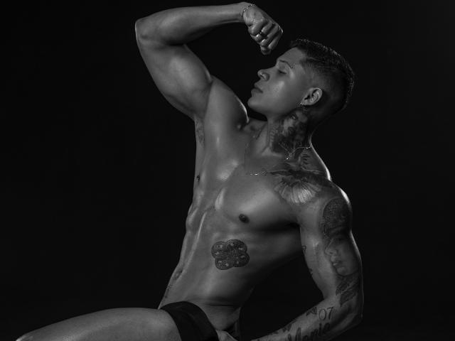 DiagoRockfield, shirtless, muscular, dark-skinned, tattoos, arm raised, eyes closed, black underwear, shiny skin, short buzzcut, side profile, black background, grayscale, photo, defined abs, sexy.