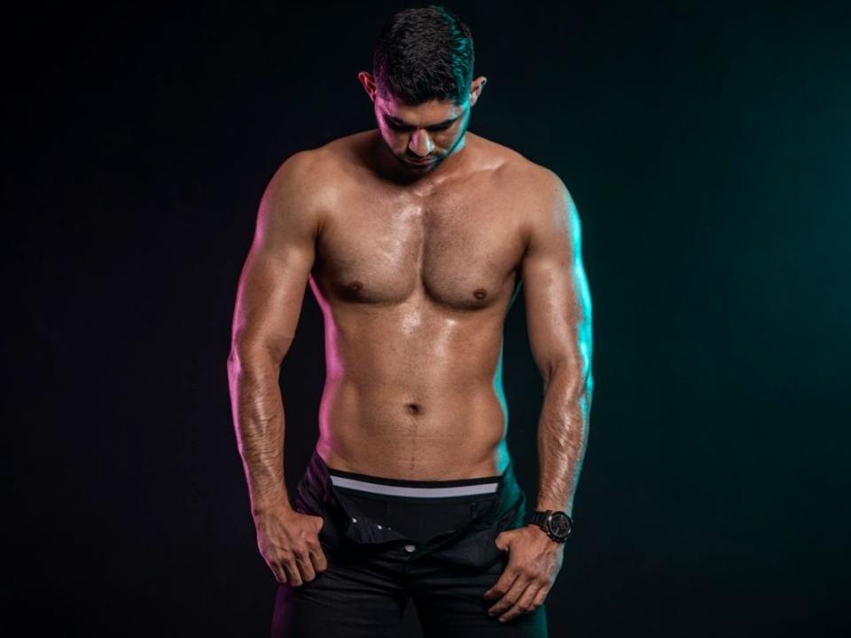 TonnyRice is a muscular, shirtless dude with a sweaty, glistening chest, dark pants, and a watch, looking down with his hands in his pants.