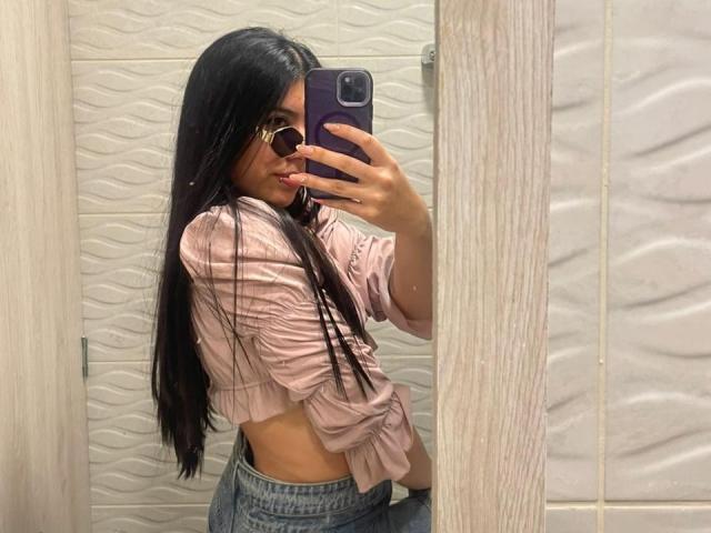 MiluSky with long black hair, wearing a pink cropped shirt, showing her small ass in tight jeans, taking a mirror selfie with a purple phone.