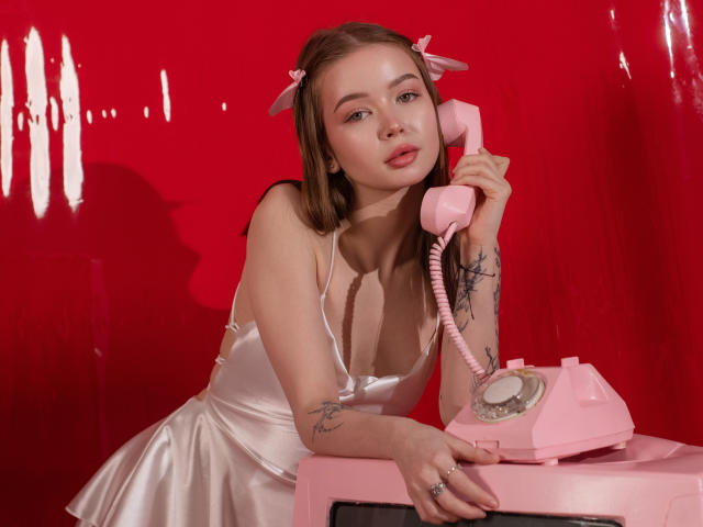 ViolettaFane with pink hair, satin dress, holding pink phone, tattoos on arm, leaning on pink phone, red background, cute face, pink ribbons in hair, looking at camera.