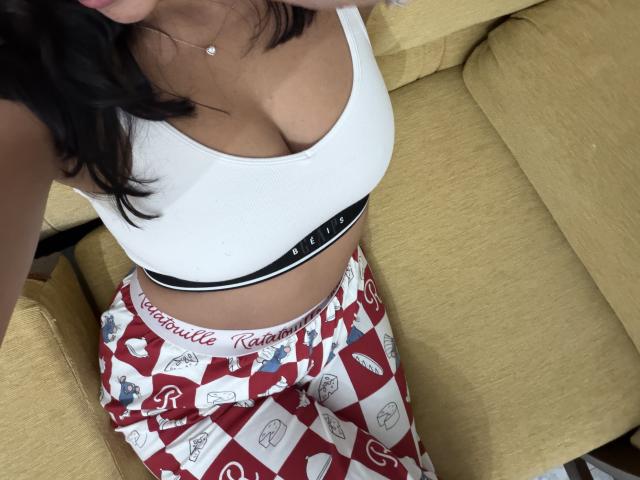 SarahPrincess has big tits in a white bra, wearing red and white checkered pajama pants with "Calvinella" waistband, sitting on a yellow couch.