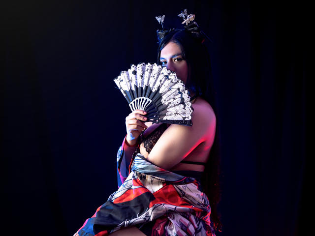 GreizSubKimura, avec ses cheveux noirs, portant un kimono, tenant un éventail décoratif, montrant ses seins, sur une photo sombre et mélancolique. Elle est partiellement masquée, avec un kimono coloré et à motifs..