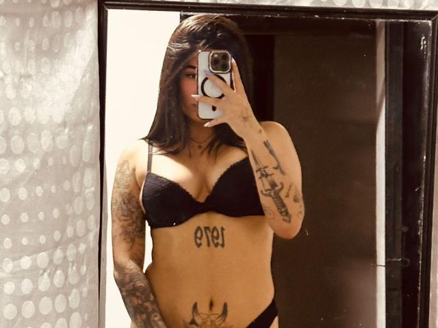 JessiParker with black bra and panties, showing tattoos on arms, chest, and belly, taking a mirror selfie with phone, brown hair, tattoos visible, mirror reflection.