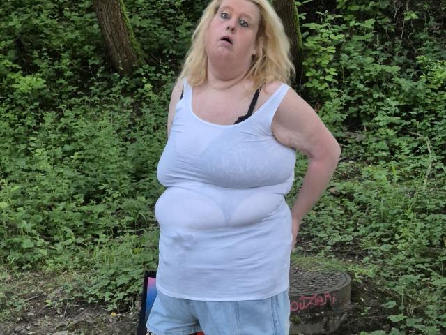 StephanieLeo69 has large, wet tits visible through a white, see-through tank top, with blue jeans, standing outdoors, looking surprised with hands on hips.