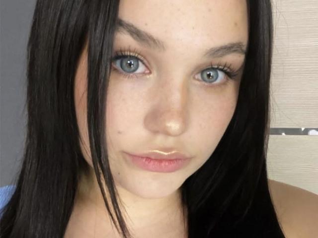 AnnyMarryah has blue eyes, straight black hair, light skin, and a slight pout with pinkish lips. Her eyebrows are dark and slightly raised. She's looking directly at the camera.