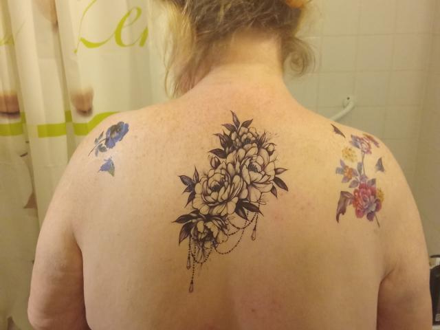 StephanieLeo69's back with three tattoos: a black floral design in the center, blue butterflies on the left, and colorful flowers on the right, all on pale skin.