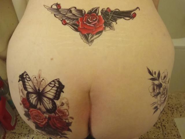 StephanieLeo69's tattooed butt with a red rose and black wings on her lower back, a black butterfly with red roses on her right butt cheek, and white flowers on left.