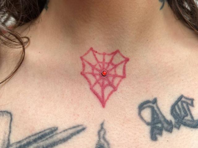 AmySpider's neck has a red spider tattoo with a small red jewel in the center, flanked by black Gothic-style tattoos on her chest.