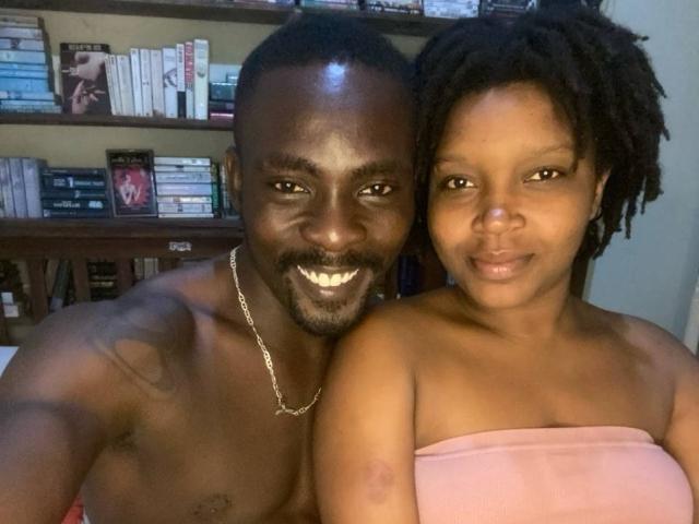 SexyAryaAlexander with dark skin and short dreadlocks, standing next to a shirtless dark-skinned SexyAryaAlexander with a silver necklace and a tattoo on his left shoulder.
