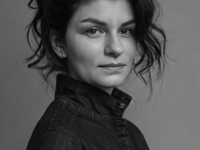 BluesStar with wavy dark hair, wearing a denim shirt, has a subtle smile and earrings, looking slightly to the side in a black-and-white portrait.