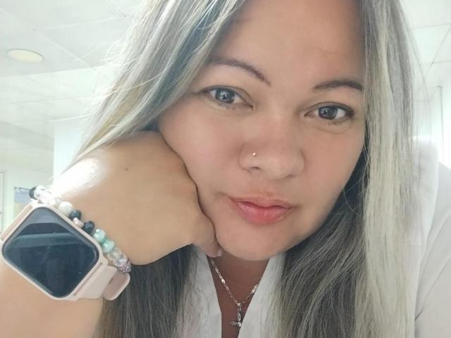 YeralGrace with pouty lips, nose piercing, and long blonde hair, wearing a pink smartwatch with colorful beads, resting her chin on her hand.