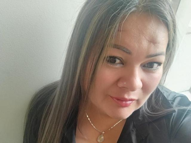 YeralGrace has light brown skin, straight brown hair with blonde highlights, and a subtle smile. She's wearing a black shirt and a gold necklace with a small pendant.