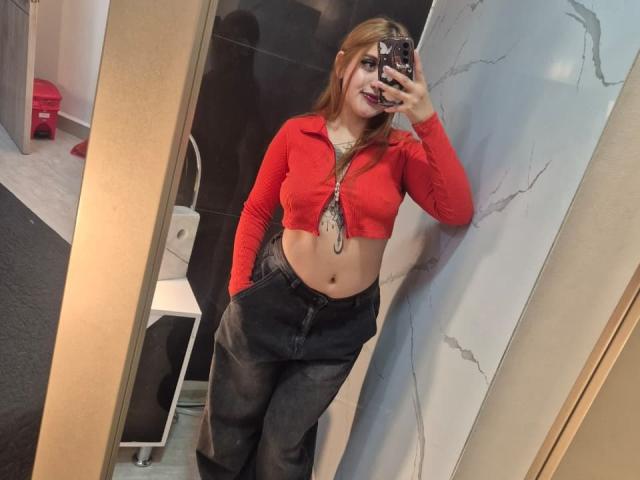 MaylinSanchez, with red cropped top showing her tits, black jeans, and long brown hair, takes a mirror selfie, holding a phone with a black and white case.