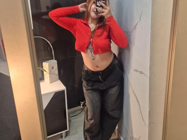 MaylinSanchez with red crop top, exposing her tits, and high-waisted dark jeans, taking a mirror selfie, showing her belly button and a necklace.