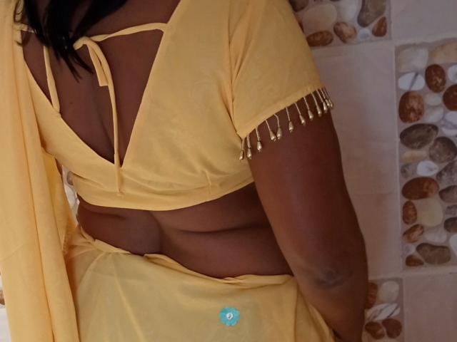 La tenue jaune d'Aadhya révèle sa silhouette foncée et voluptueuse, avec un ventre et des bras apparents. Elle porte de petits ornements en perles dorées sur sa manche et un tissu jaune qui recouvre ses parties intimes..