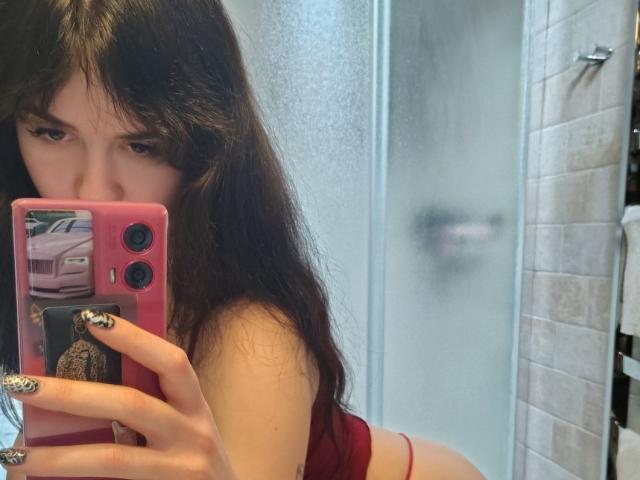 BerryDiva with long dark brown hair, wearing a red top, holding a pink phone with tiger-print nails, taking a mirror selfie, showing her ass in the reflection.