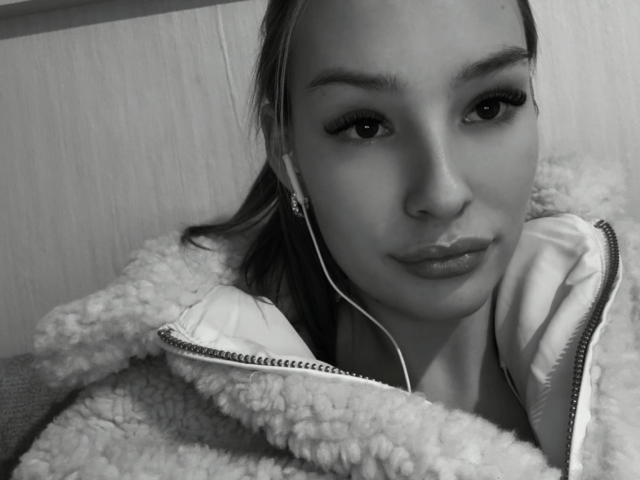 AngelaLuxe, black and white selfie, wearing fluffy zip-up jacket, headphones in, pouty lips, slightly parted, long eyelashes, straight hair, wooden wall background, casual, cute, soft texture.