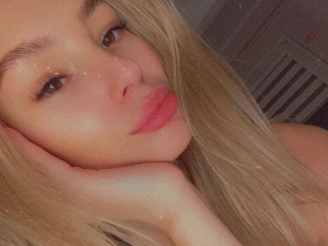 AngelaLuxe's face, blonde hair, brown eyes, and pink lips with her hand on her cheek, showing off her cute, sexy, and attractive look. Her tits are not visible.