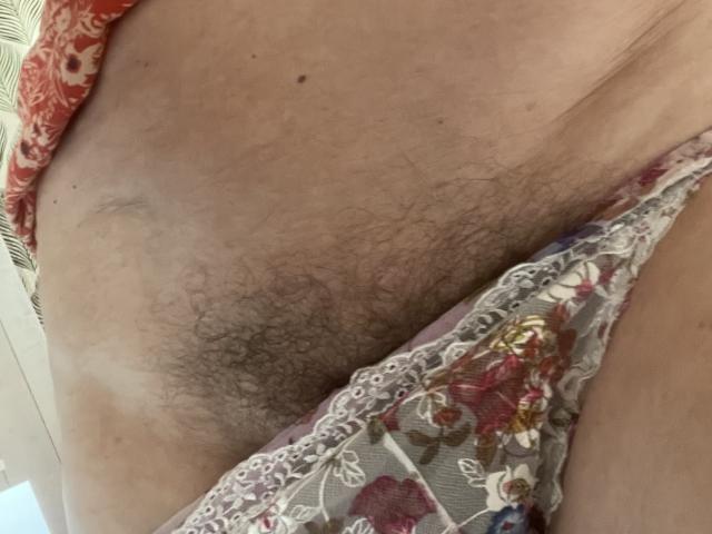 La vellosa vulva de Bourgeoisex, visible a través de la ropa interior de encaje floral, con tela estampada de color rojo en el lateral. Toma de primer plano..
