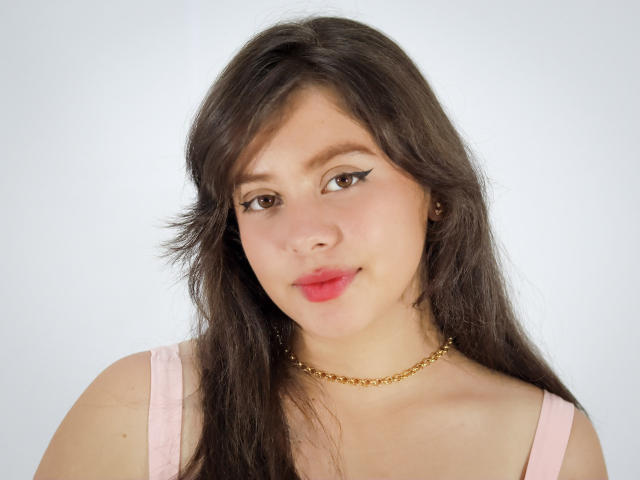 SophieMonAmour has brown hair, light skin, and wears a pink top with a gold chain necklace. She has black eyeliner, pink lipstick, and a slight smile.