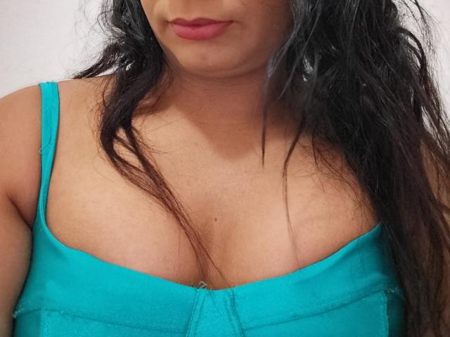 Aripietra with dark hair, red lipstick, and a teal bra showing her tits, slightly messy hair, tan skin, and a subtle smile. No visible background.