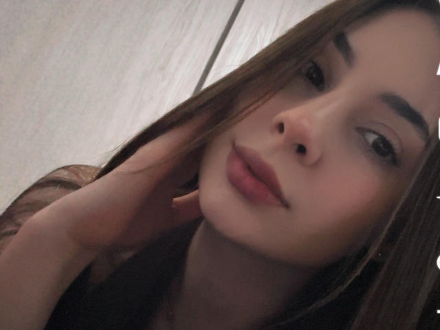 NikoleFoster's face with brown hair, slightly parted lips, and a hand touching her cheek, showing a relaxed and gentle expression. She has a cute, natural look.