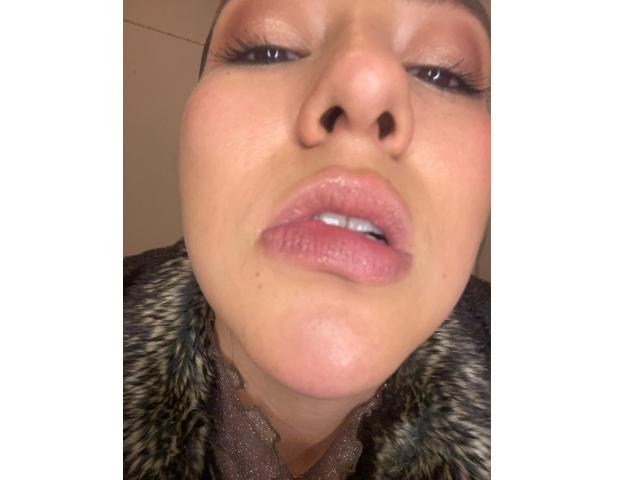 Velka's face with puffy pink lips, slightly parted, brown eyes with long lashes, and a fur-lined jacket collar, looking down with a soft, somewhat sexy expression.