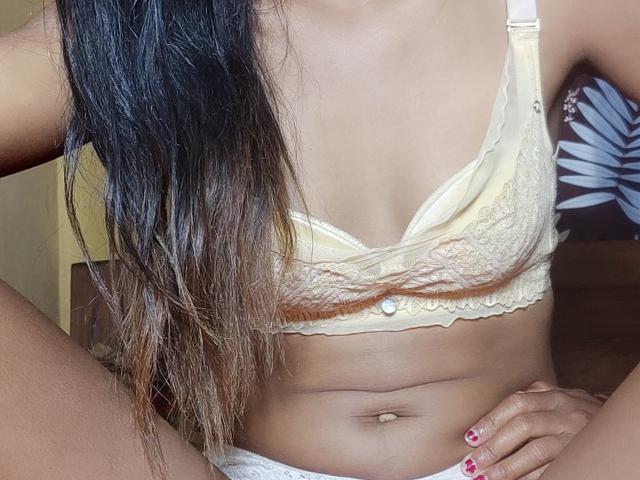 LoderFist's tits in a yellow lace bra, flat stomach, and long dark brown ombre hair, sitting with hands on her hip. Her navel is visible, nails painted pink.