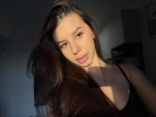 DanyellEden's face with long brown hair, brown eyes, and pink lips, wearing a black tank top, sunlight on her face, soft shadow, necklace with small cross.