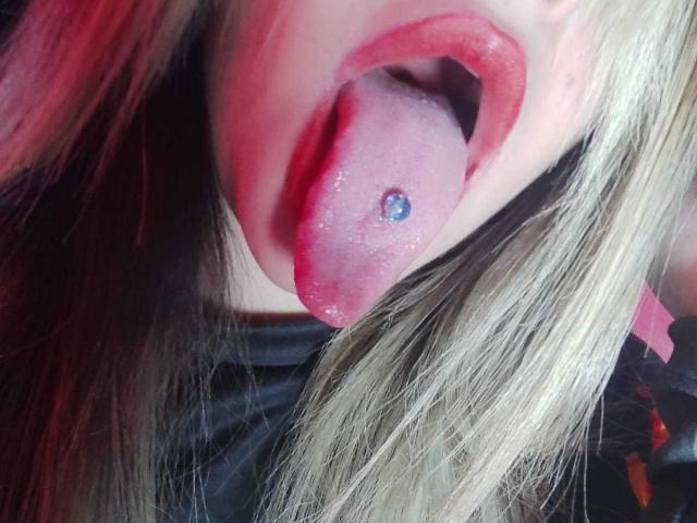 AshGraven's tongue is out with a blue ball-trail piercing. She's got glossy red lips and blonde hair. Her tongue is slightly wet and her lips are parted.