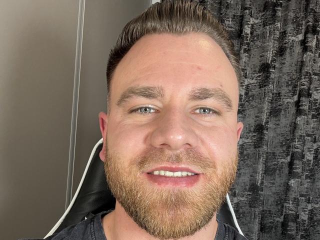 Thori69 has a chubby face, short brown hair, a full beard, and is smiling with white teeth. He's wearing a black shirt and has blue eyes.