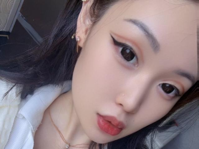 YukiiTyan's face, pale skin, black hair, winged eyeliner, red lipstick, nose piercing, small earrings, white shirt, slightly parted lips, looking at camera, soft light, subtle makeup.
