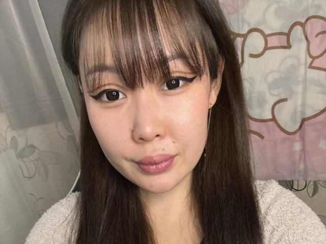 YukiiTyan has straight brown hair, bangs, black eyeliner, a nose ring, and is wearing a white towel. Her pink lips are slightly parted, and she's looking at the camera.