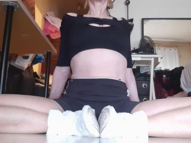 IssahneMay is sitting with legs spread, wearing a black crop top and black shorts, exposing her white sneakers and showing her toned midriff and small tits.