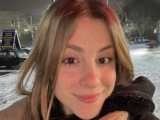 KerryColver with light brown hair, fair skin, and a subtle smile, holding a black scarf, snowflakes on her face, and a street in the background at night.