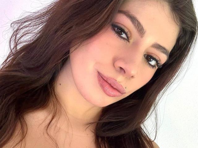 LindaMancini has brown wavy hair, full pink lips, and brown eyes with long lashes. She's smiling softly with a small nose piercing on her left side.
