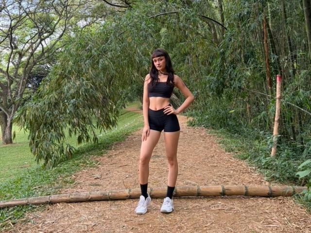 CandyyClair stands on a dirt path, wearing a black sports bra, black shorts, black socks, and white sneakers, with her hand on her hip, and her ass slightly exposed.