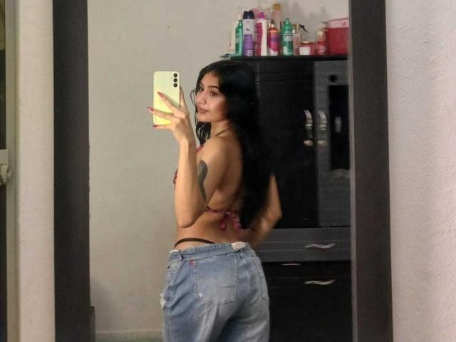 NicolleSweetty in a mirror selfie, wearing a red string bikini top and blue jeans, showing her back and ass, with long black hair, holding a yellow phone.