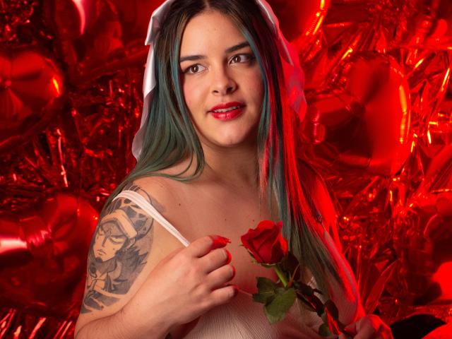 AuroraSantorini mit rotem Lippenstift, grünen Haaren, weißem Kleid, die eine rote Rose hält, mit einem Tattoo am rechten Arm, roten Ballons, lächelnd, mit einem weißen Schleier, die eine Rose mit der rechten Hand hält, rote Fingernägel..