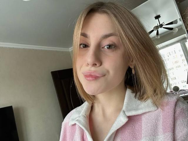 KerryColver with light brown hair, pink and white striped shirt, white collar, subtle smile, pink lips, light skin, small nose, brown eyes, in a room with ceiling fan.
