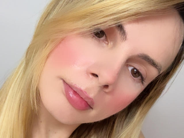 BellaCampos has pink blushed cheeks, glossy pink lips, and blonde hair with a slight side part, looking softly at the camera with brown eyes.