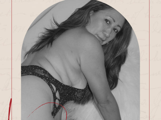 LizaMintelli, topless, lying on a bed with long dark hair, wearing a sparkly black thong, looking back at the camera, showing her ass and a slight smile.