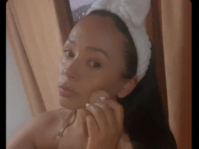 LuluSinclair has a towel on her head, glistening skin, and is touching her cheek with a hand. She's looking at the camera with a slight pout.